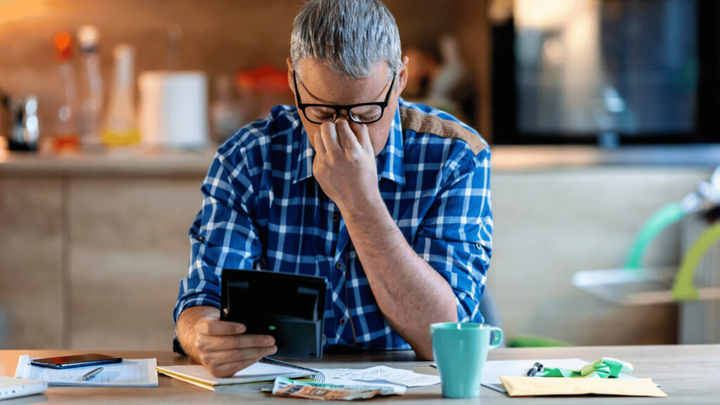 A man sitting at a table with their head in their hands, pondering renting a coworking space due to economic uncertainty instead of a traditional office.
